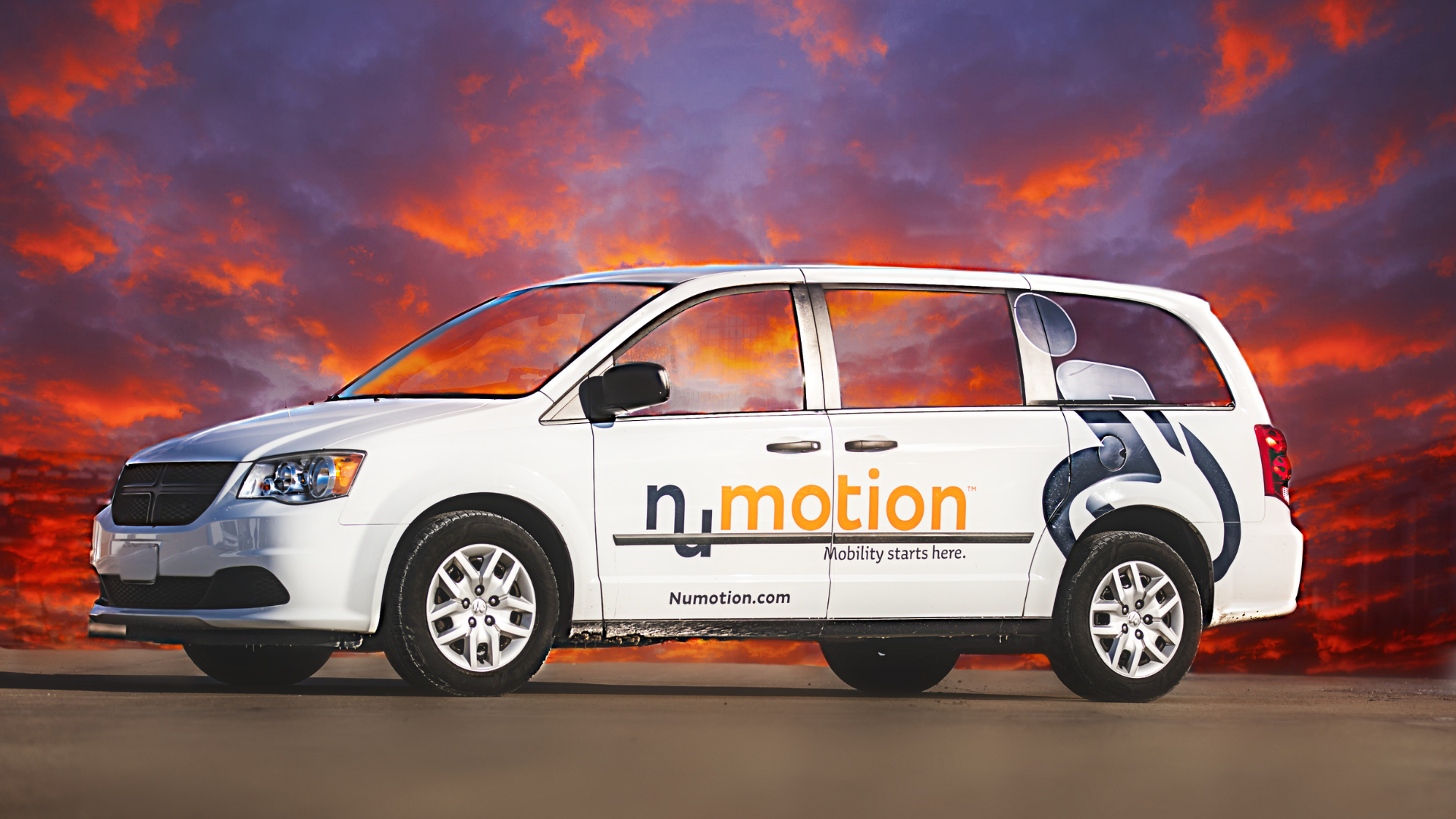 A white minivan with Numotion branding and the slogan Mobility starts here is parked on pavement, with a dramatic sunset sky in the background. The van offers home delivery, making accessibility more convenient.