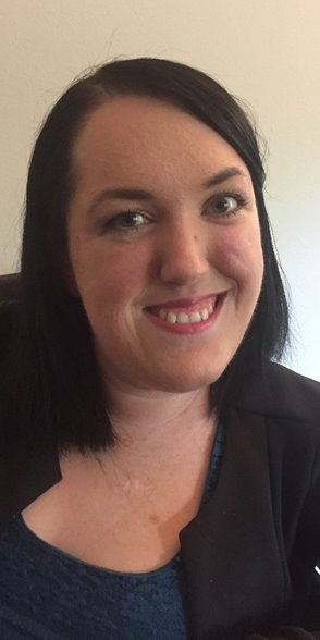 Gabriellas Story: A woman with straight black hair, wearing a dark blazer over a blue top, smiles at the camera in front of a plain light background.