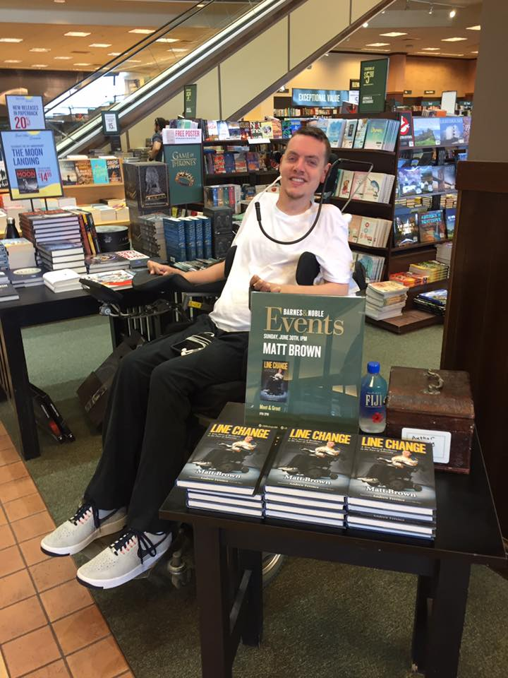 A man sits behind a table with stacks of books titled Line Change at a bookstore event, sharing Matts Story. A sign displays Events: Matt Brown Live, with bookshelves and store displays visible in the background.
