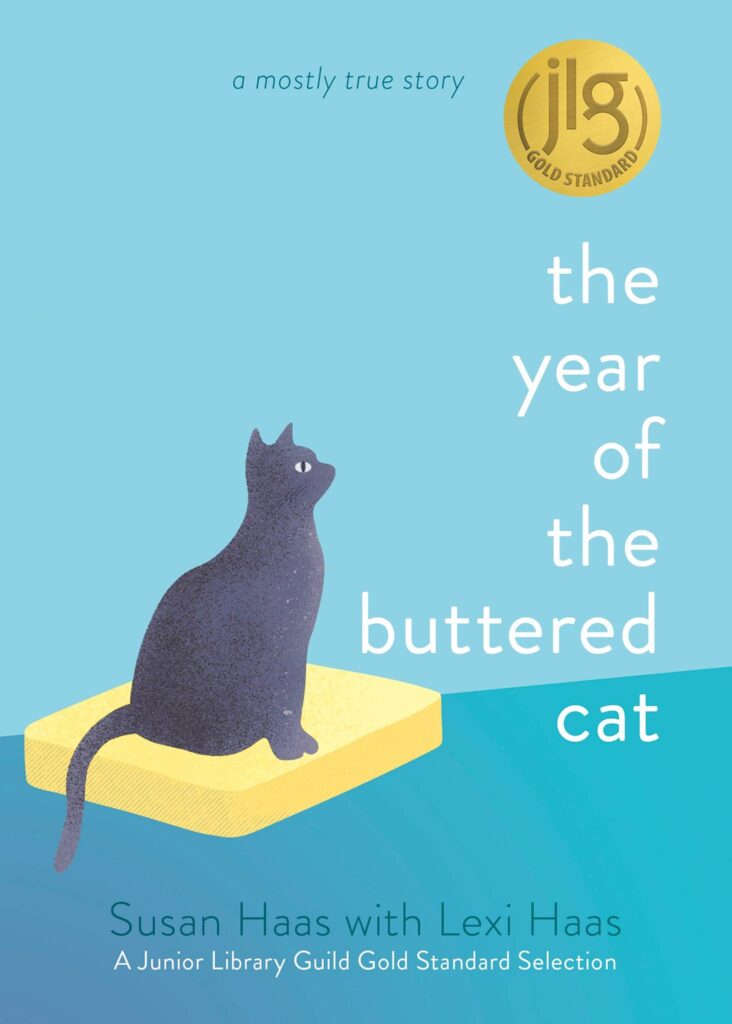 Book cover shows a dark gray cat sitting on a stick of butter against a light blue background. The title reads “the year of the buttered cat”—Lexis Story by Susan Haas with Lexi Haas. A gold Junior Library Guild medal is in the corner.