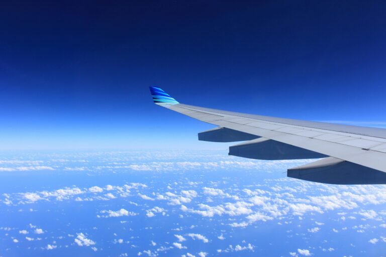 View from an airplane window showing the plane’s wing above a layer of fluffy white clouds and a deep blue sky, capturing the joy of accessible travel.