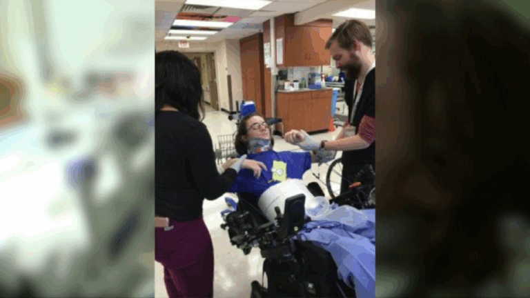 Ryans Story: A person in a wheelchair, wearing a neck brace, is assisted by two people in a medical facility, helping adjust the persons arm and blood pressure cuff. The setting appears to be a hospital or rehab center.