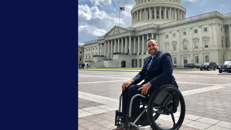 A man in a wheelchair smiles at the camera outside the U.S. Capitol on a sunny day, an American flag flying in the background—capturing a moment from Justins Story.