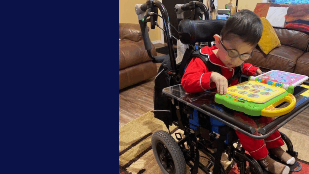 A young child, part of Jakes Story, wears glasses and a red outfit while playing with a colorful electronic learning toy on a tray table in a cozy living room.