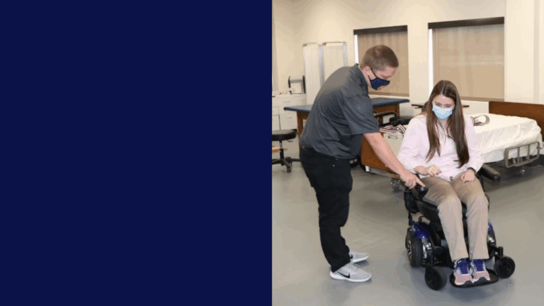 Aarons Story: A man assists a woman in a power wheelchair indoors near a hospital bed. Both wear masks and casual clothing, suggesting the setting is a rehabilitation or medical facility.