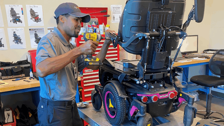 A technician in a gray uniform uses a drill to repair a motorized wheelchair in a workshop with tools and red toolboxes, capturing a moment from Daniels Story.