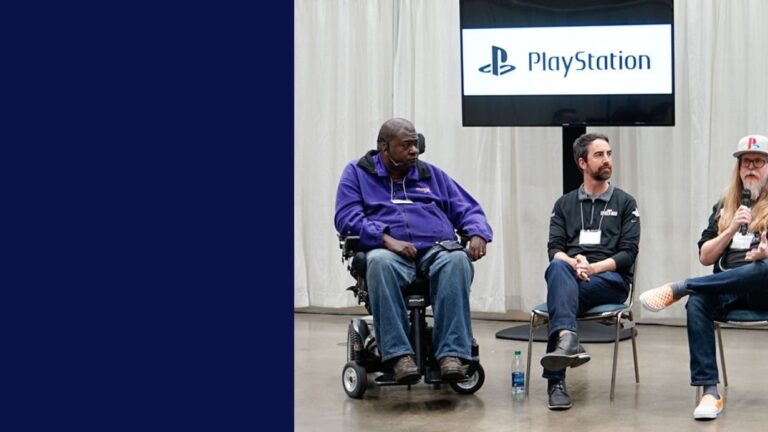 Three men sit on a panel in front of a PlayStation logo; one uses a wheelchair, another has a beard and dark shirt, and the third wears a hat and glasses. They share insights at an event with a white curtain backdrop, discussing Pauls Story.
