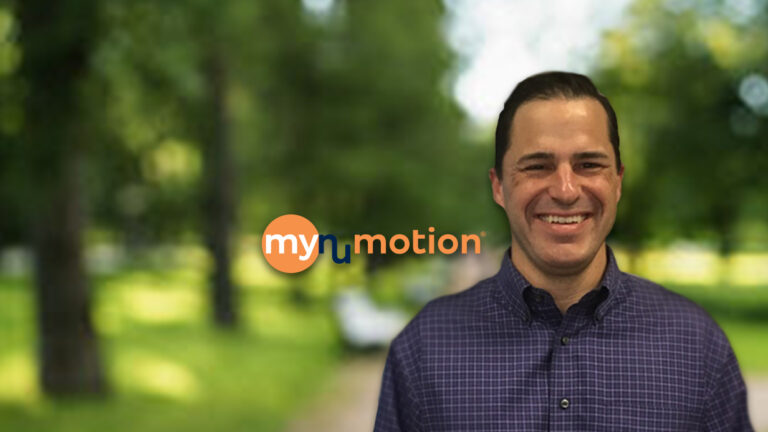 A smiling man in a purple checkered shirt stands in front of a blurred green outdoor background with the mynumotion logo next to him, sharing Mikes Story.