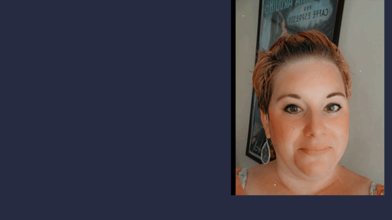 A woman with short, light brown hair and hoop earrings smiles at the camera. She is indoors, and a framed sign is visible in the background on the wall. The left side shows a solid dark blue color, highlighting Aubreys Story.