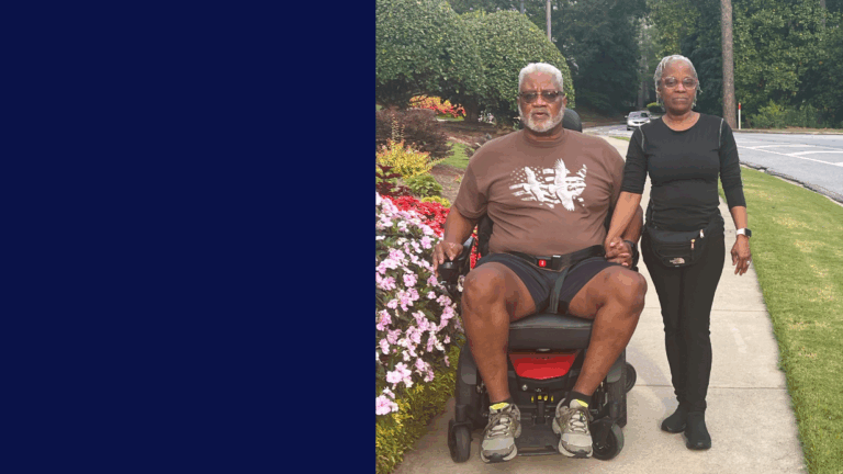 A man in a wheelchair and a woman holding hands walk along a sidewalk in Richmond, bordered by colorful flowers and greenery, with trees and a road in the background. A solid navy blue panel fills the left side of the image, adding depth to their story.