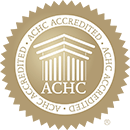Gold seal with the words ACHC ACCREDITED repeated around the edge, featuring a central image of a building with pillars above the letters ACHC, symbolizing quality and trust.
