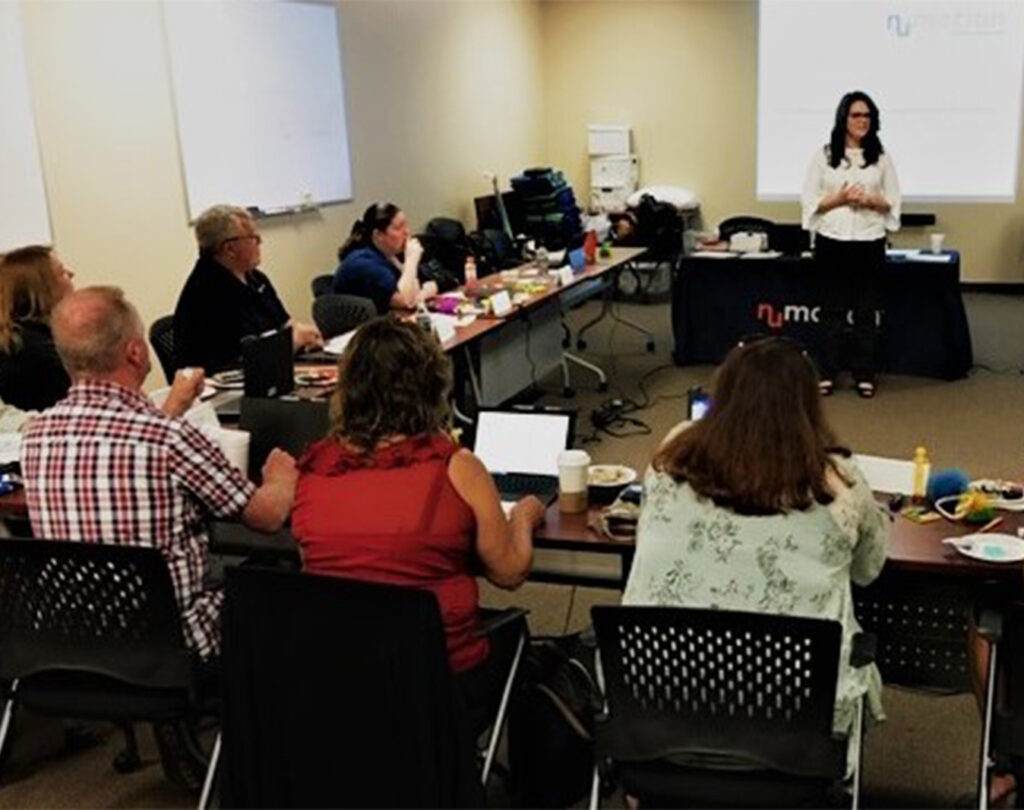 A woman presents to a group in a conference room as part of the ATP Development Program, with notepads, laptops, and food on tables. A projector screen and whiteboards are visible in the background.