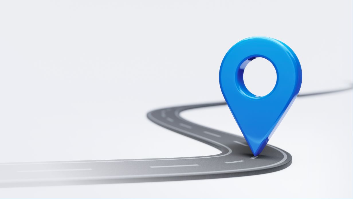 A large blue map pin marker stands on a winding, empty road with white lane markings, set against a plain light background, representing a clear path for navigating the insurance appeals process.