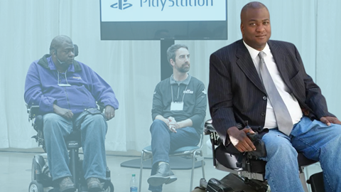 A man in a suit and jeans sits in a power wheelchair, superimposed over a faded background showing two men in wheelchairs and Paul Amadeus Lane on a chair in front of a PlayStation sign, offering a unique perspective.