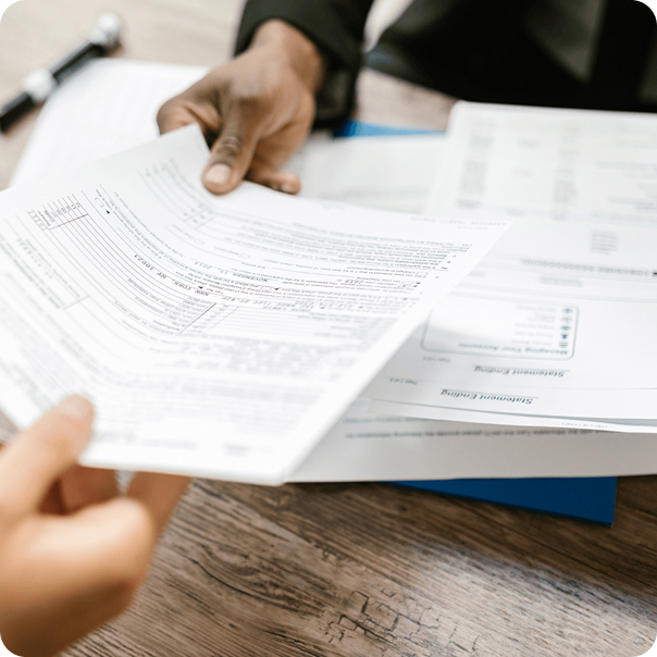 Two people review and exchange paperwork at a wooden desk, with forms and a pen visible, highlighting an order process or timeline in a business or financial meeting.