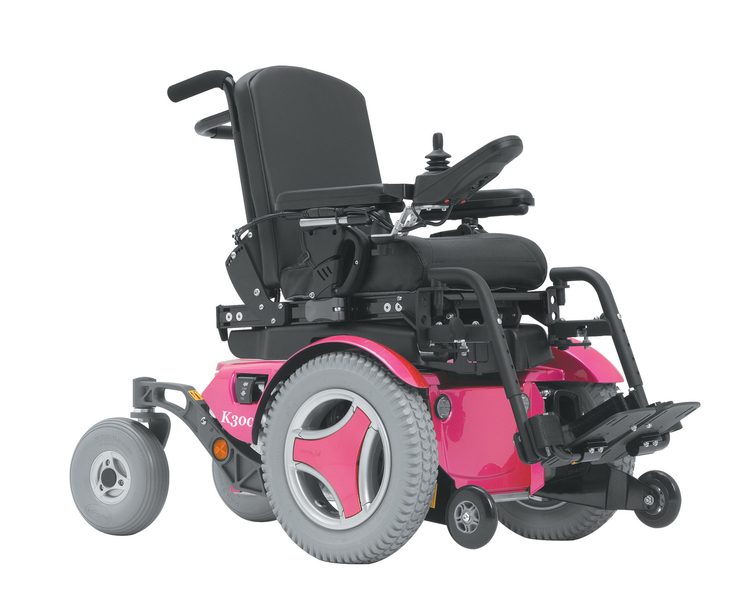 A pink and black pediatric power wheelchair with large rear wheels, padded seat and backrest, adjustable armrests, footrests, and a joystick control on the right armrest. Ideal for comfort and mobility for younger users.